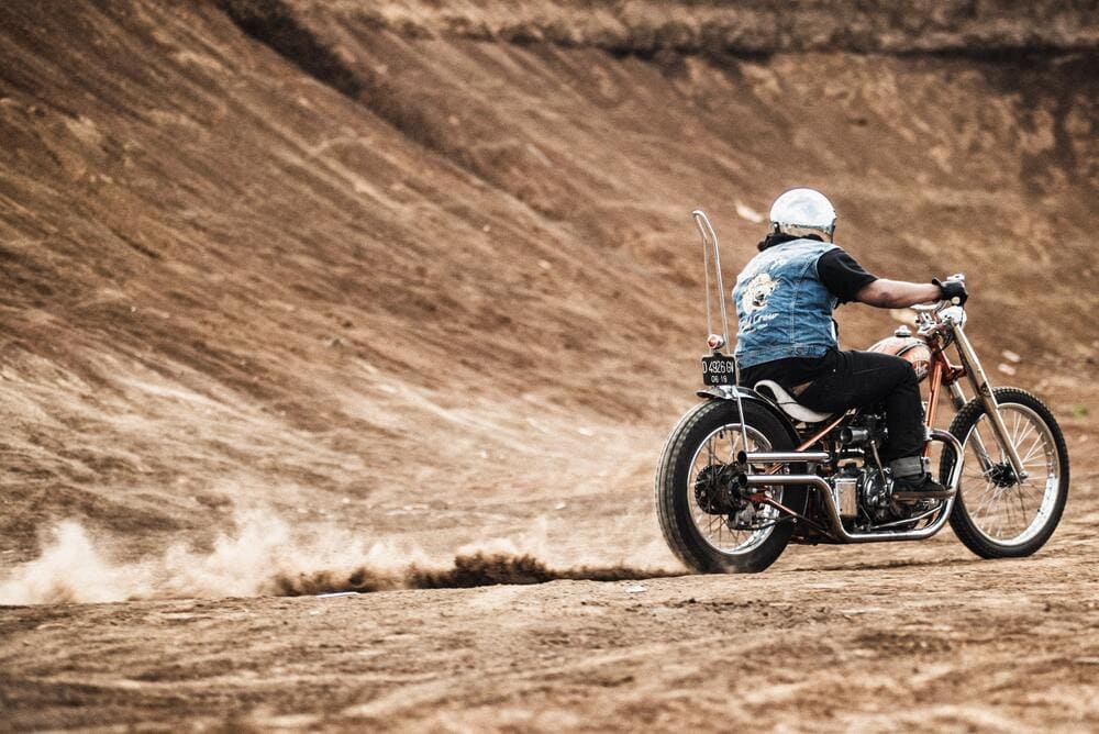 Man in sleeveless denim jacket riding motorcycle in the dirt