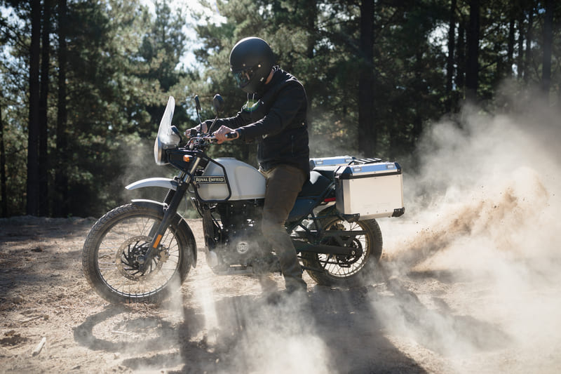 side profile shot of a man with a motorcycle helmet and a cool denim motorcycle jacket, riding a motorbike with dust in the air